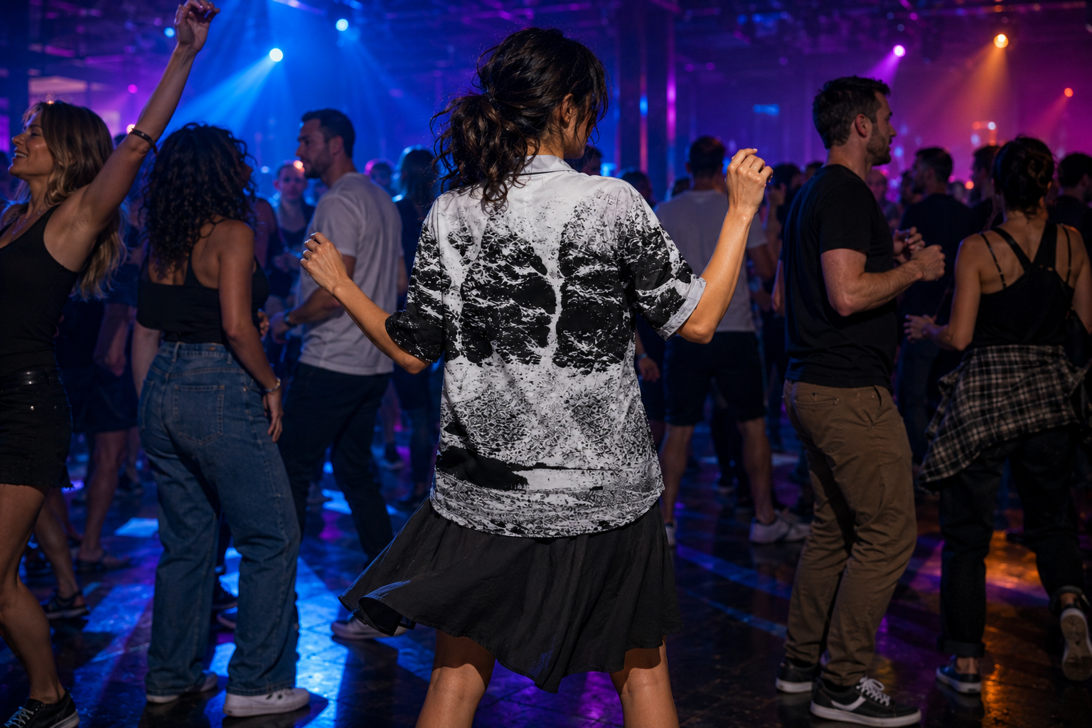 Woman dancing on a nightclub floor under blue and purple lights, wearing a black and white Arctropic shirt with a breaking wave print.